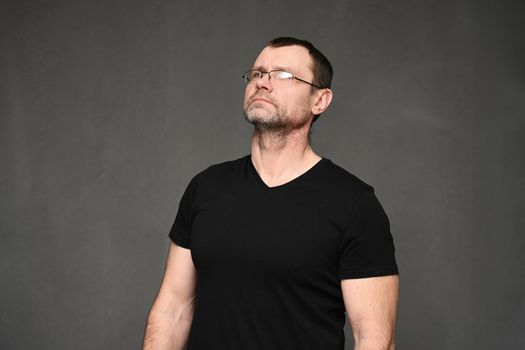 Adult caucasian man in a t-shirt and glasses looks up simply