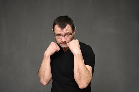 Adult man in a black t-shirt and glasses shows boxing with his hands