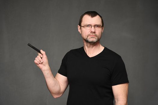 An adult man in a black T-shirt and glasses points to the side with a pen