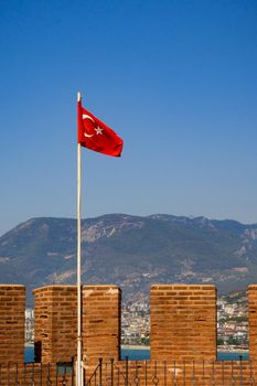 The waving flag of Turkey. Against the background of the Alanian fortress, Ich Kale and the mountains.