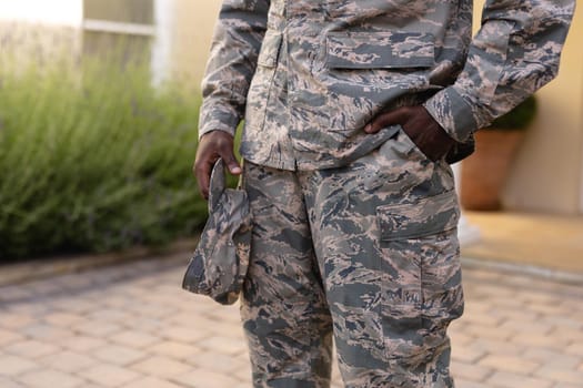 Midsection of male african american soldier holding cap standing with hand in pocket. identity and patriotism, unaltered.