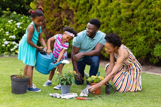 Happy african american family watering plants together in garden. family, love and togetherness concept, unaltered.