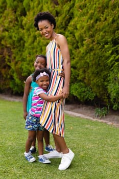 Full length portrait of smiling african american woman embracing daughters at garden. family, love and togetherness concept, unaltered.
