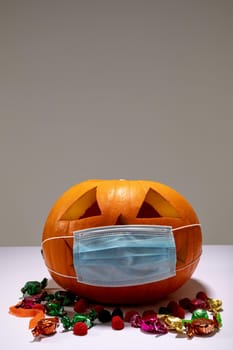 Halloween jack o lantern with face mask on grey background with sweets. halloween tradition and celebration during covid 19 pandemic concept digitally generated image.