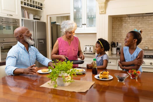African american grandmother serving breakfast for her two granddaughters in the kitchen at home. family, love and togetherness concept, unaltered.