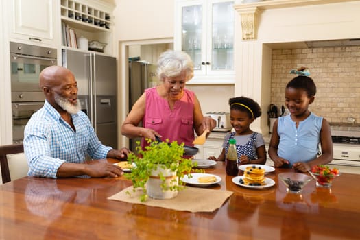 African american grandmother serving breakfast for her two granddaughters in kitchen at home. family, love and togetherness concept, unaltered.