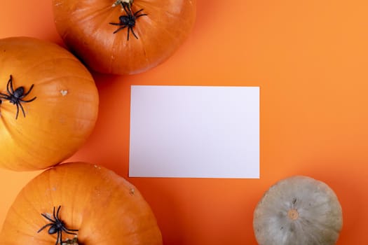 Composition of halloween decoration with pumpkins and sheet with copy space on orange background. horror, fright, halloween tradition and celebration concept digitally generated image.