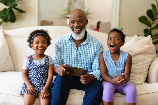 African american grandfather and his two granddaughters with digital tablet smiling at home. family, love and technology concept, unaltered.