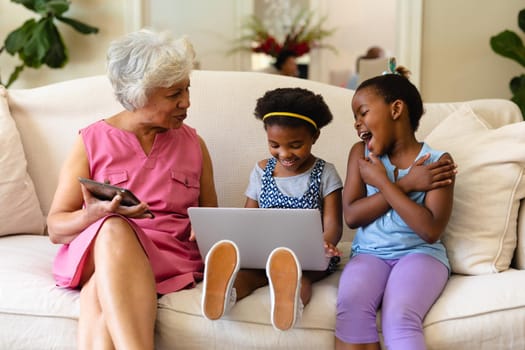 African american grandmother and her two granddaughters using laptop sitting on couch at home. family, love and technology concept, unaltered.