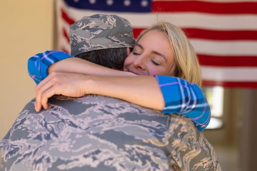 Blond caucasian woman hugging army soldier on his return home against usa flag. people, love and patriotism, unaltered.