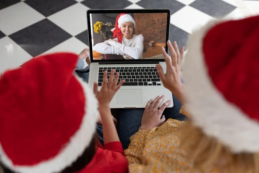 Caucasian woman with her daughter at home at Christmas, using laptop computer, video chatting with another woman. Social distancing during Covid 19 Coronavirus quarantine lockdown.