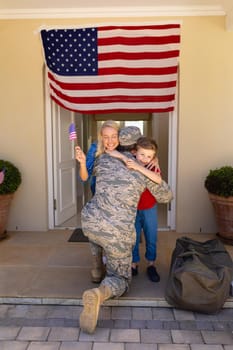 Caucasian woman and son with usa flag hugging army soldier on his return at the entrance. family, love and patriotism concept, unaltered.