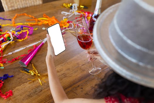 Cropped image of biracial young woman with smart phone enjoying party on video call, copy space. unaltered, wireless technology, video call and distant party celebration.