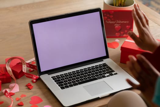 African american woman waving on valentine's video call through laptop showing copy space by gifts. technology, lifestyle and surprise, unaltered.