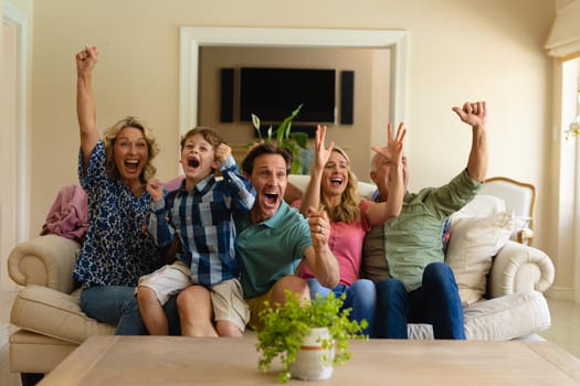 Caucasian three generation family cheering while watching tv sitting together on the couch at home. family and entertainment concept, unaltered.