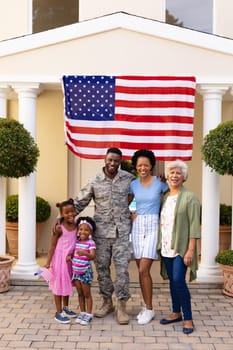 Portrait of smiling african american family with army soldier at entrance against usa flag. bonding and patriotism, unaltered.