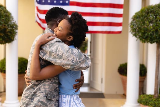 Side view of happy african american woman embracing military soldier at house entrance. togetherness, bonding and patriotism, unaltered.