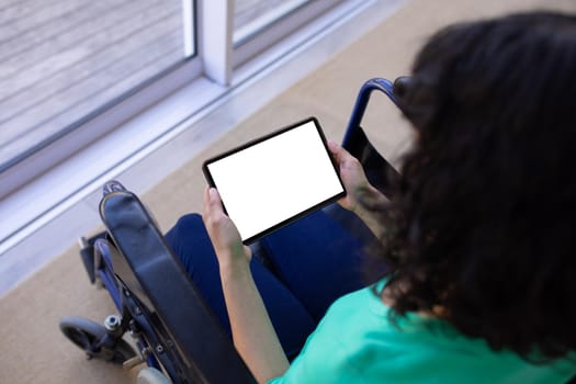 High angle view of biracial disabled woman on wheelchair using tablet pc with copy space on blank. technology and disability, unaltered.