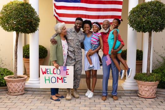 Portrait of smiling african american family standing with placard at house entrance. bonding and patriotism, unaltered.