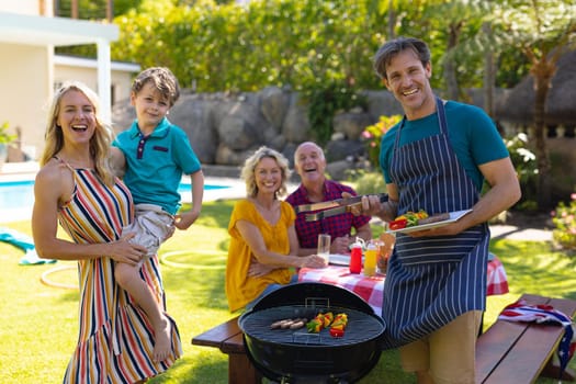 Portrait of cheerful caucasian family barbecuing together in the garden. family, togetherness and weekend lifestyle concept, unaltered.