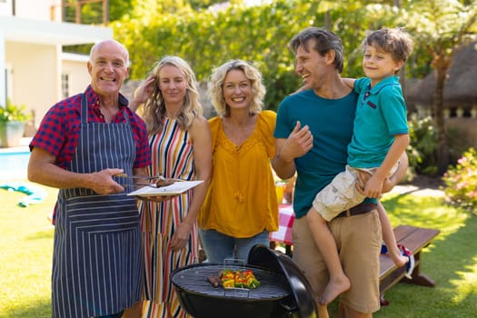 Portrait of smiling caucasian three generational family barbecuing together in the garden. family, togetherness and weekend lifestyle concept, unaltered.