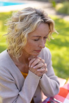 Blond senior caucasian woman with eyes closed and hands clasped praying in garden. people and spirituality concept, unaltered.