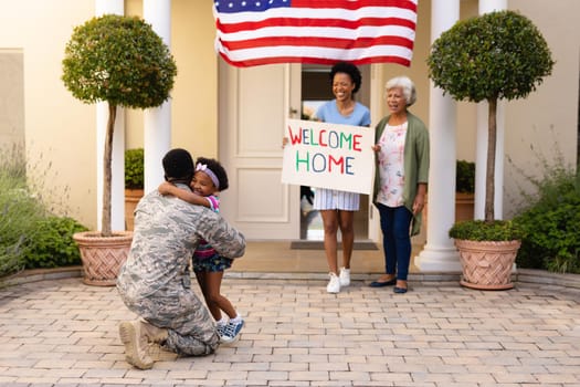 Smiling african american women looking at girl embracing father soldier's return home at entrance. family, bonding and patriotism, unaltered.
