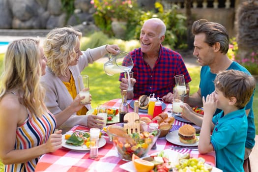 Cheerful caucasian three generational family enjoying lunch at table in garden. family, togetherness and weekend lifestyle concept, unaltered.