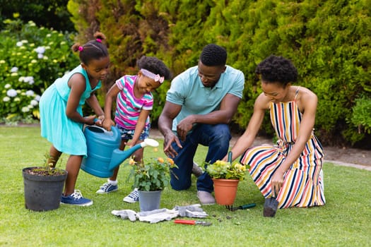 African american family watering plants together in backyard garden. family, love and togetherness concept, unaltered.