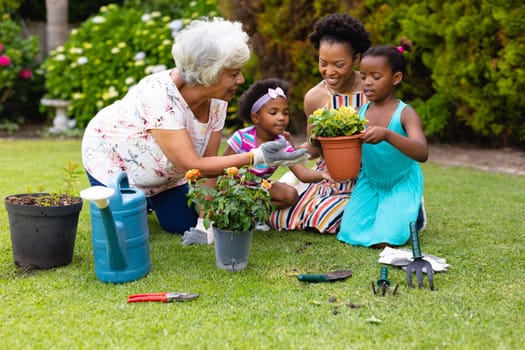 African american senior woman teaching gardening to grandchildren and daughter at backyard. family, love and togetherness concept, unaltered.