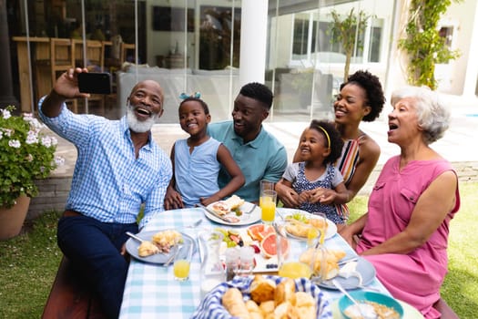 African american senior man smiling while taking selfie with family at dining table during brunch. family, love and togetherness concept, unaltered.
