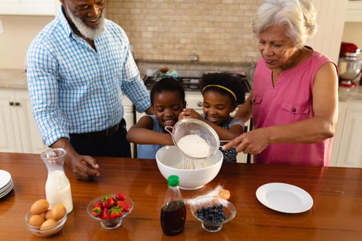 African american grandparents and two granddaughters baking together in the kitchen at home. family, love and togetherness concept, unaltered.