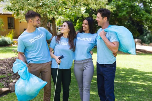 Happy multiracial volunteers collecting garbage in plastic bags during cleanup in park. environmental cleanup, social issues, responsibility and recycling concept.