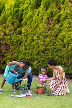 Full length of happy african american family watering plants together in backyard garden. family, love and togetherness concept, unaltered.