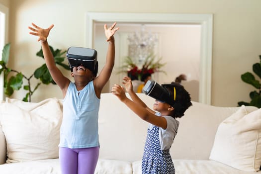 Two african american sisters wearing vr headset gesturing at home. virtual reality and futuristic technology concept, unaltered.