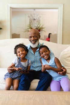 African american grandfather and two granddaughters with digital tablet smiling at home. family, love and technology concept, unaltered.
