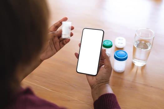 Senior woman with medicine using smart phone during online doctor consultation at home, copy space. lifestyle, wireless technology, telemedicine and healthcare.