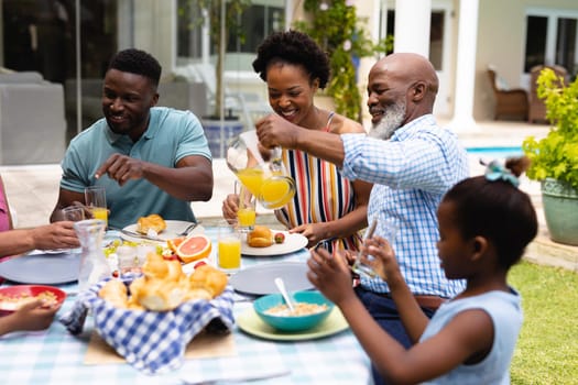 Happy african american family eating brunch at dining table in backyard. family, love and togetherness concept, unaltered.