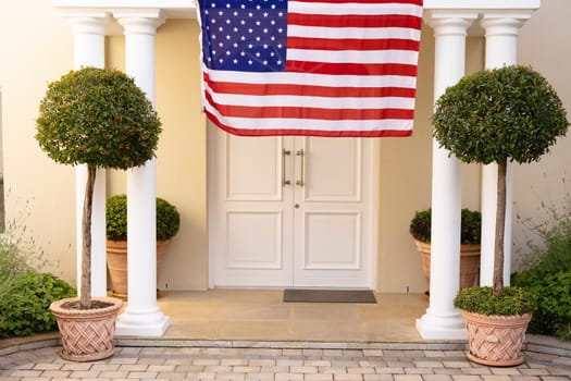 America flag hanging amidst plants at front entrance of house. patriotism, identity and home, unaltered