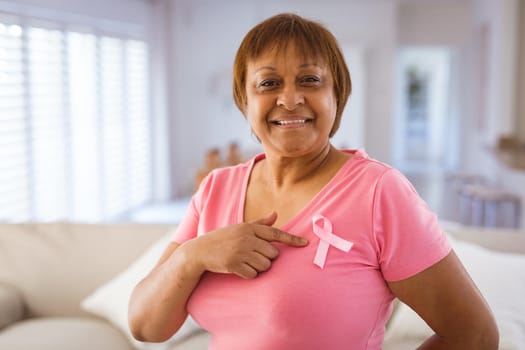 African american senior woman pointing at breast cancer awareness ribbon on pink t-shirt. identity and breast cancer awareness concept.