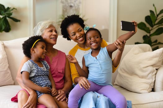 African american grandmother, mother and two granddaughters taking a selfie sitting on couch. family, love and togetherness concept, unaltered.