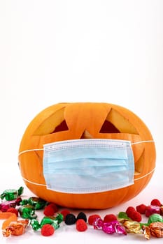 Halloween jack o lantern with face mask on white background with sweets. halloween tradition and celebration during covid 19 pandemic concept digitally generated image.
