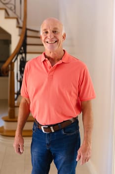 Portrait of caucasian senior man smiling while standing in the living room at home. people and emotions concept, unaltered.