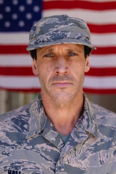 Portrait of confident army soldier wearing cap and camouflage uniform against usa flag. people, patriotism and identity concept, unaltered.