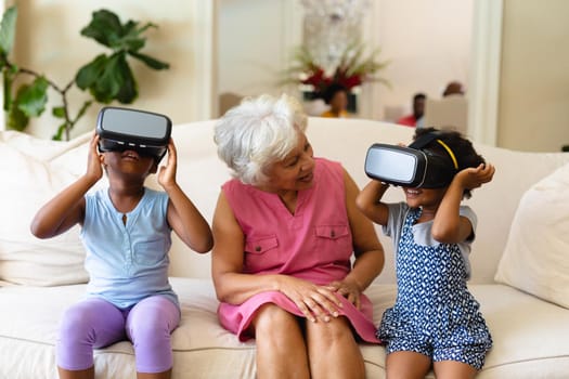 African american grandmother watching her two granddaughters wearing vr headsets at home. virtual reality and futuristic technology concept, unaltered.