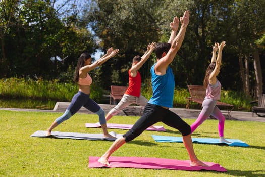 Full length of men and women with arms raised practicing yoga on exercise mats in park. healthy lifestyle and body care.