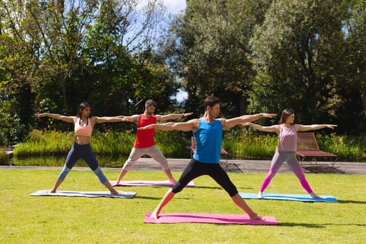Full length of men and women practicing yoga on exercise mats in public park on sunny day. healthy lifestyle and body care.