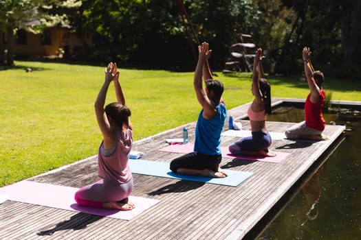 Men and women with arms raised and hands clasped practicing yoga on floorboard in park. healthy lifestyle and body care.