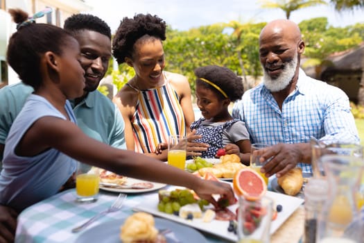 Happy african american family eating brunch at dining table in backyard. family, love and togetherness concept, unaltered.