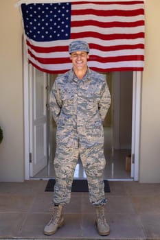 Full length portrait of smiling caucasian army soldier standing against usa flag at entrance. people, patriotism and identity concept, unaltered.